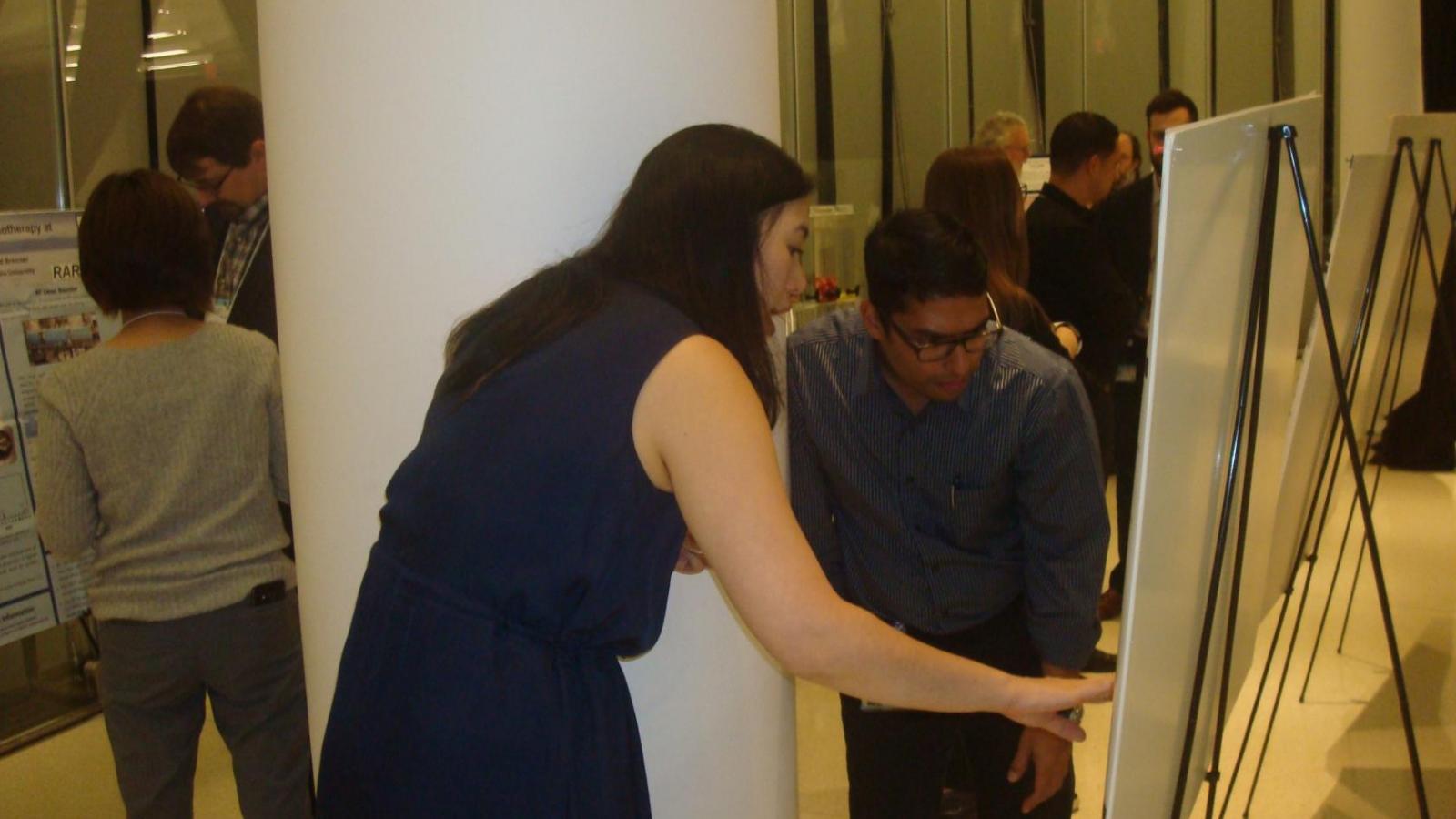 A female and male doctor discuss data being displayed on a research poster