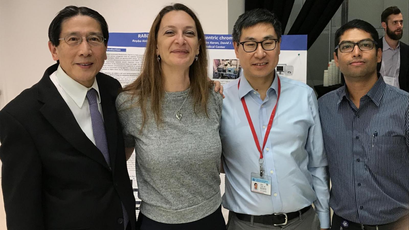 four doctors stand next to each other to take picture in front of a scientific research poster