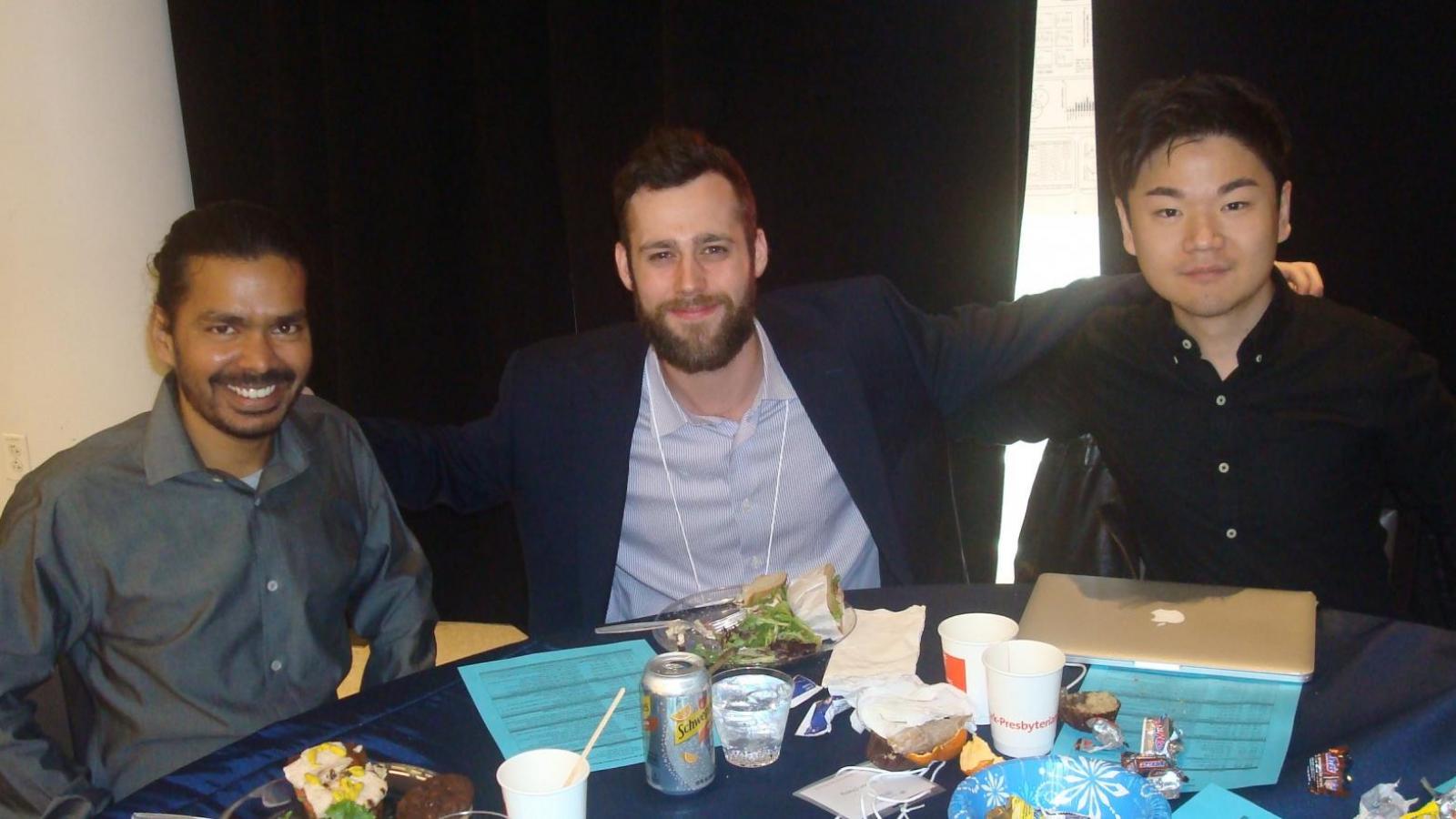 3 male doctors posing for picture at table with blue table cloth and black curtains behind them