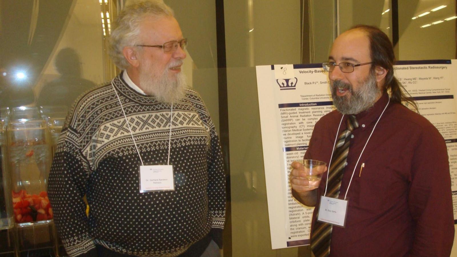 2 male doctors having a conversation over drinks while standing in front of a research poster