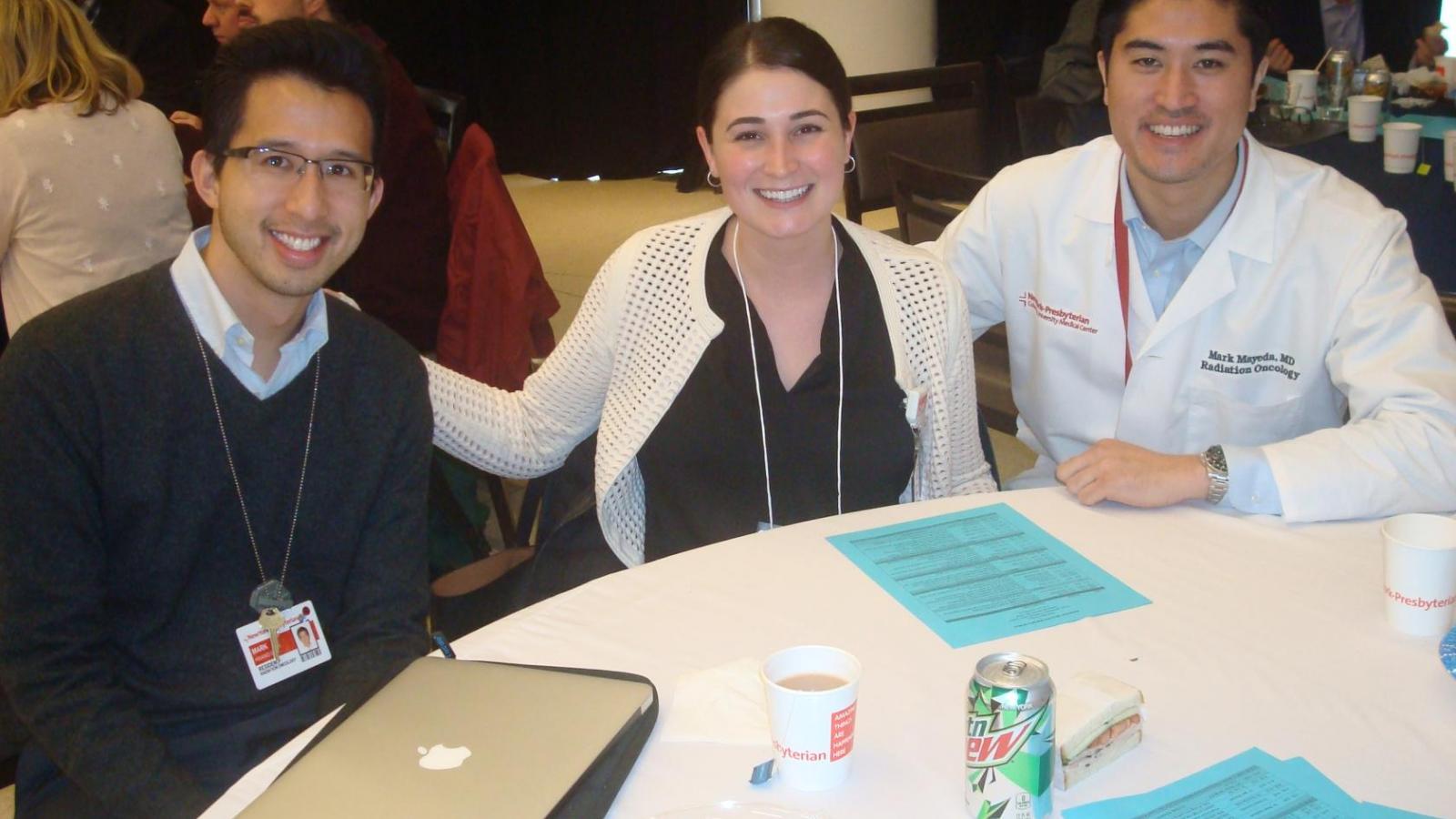 3 doctors posing for picture while seated at a table
