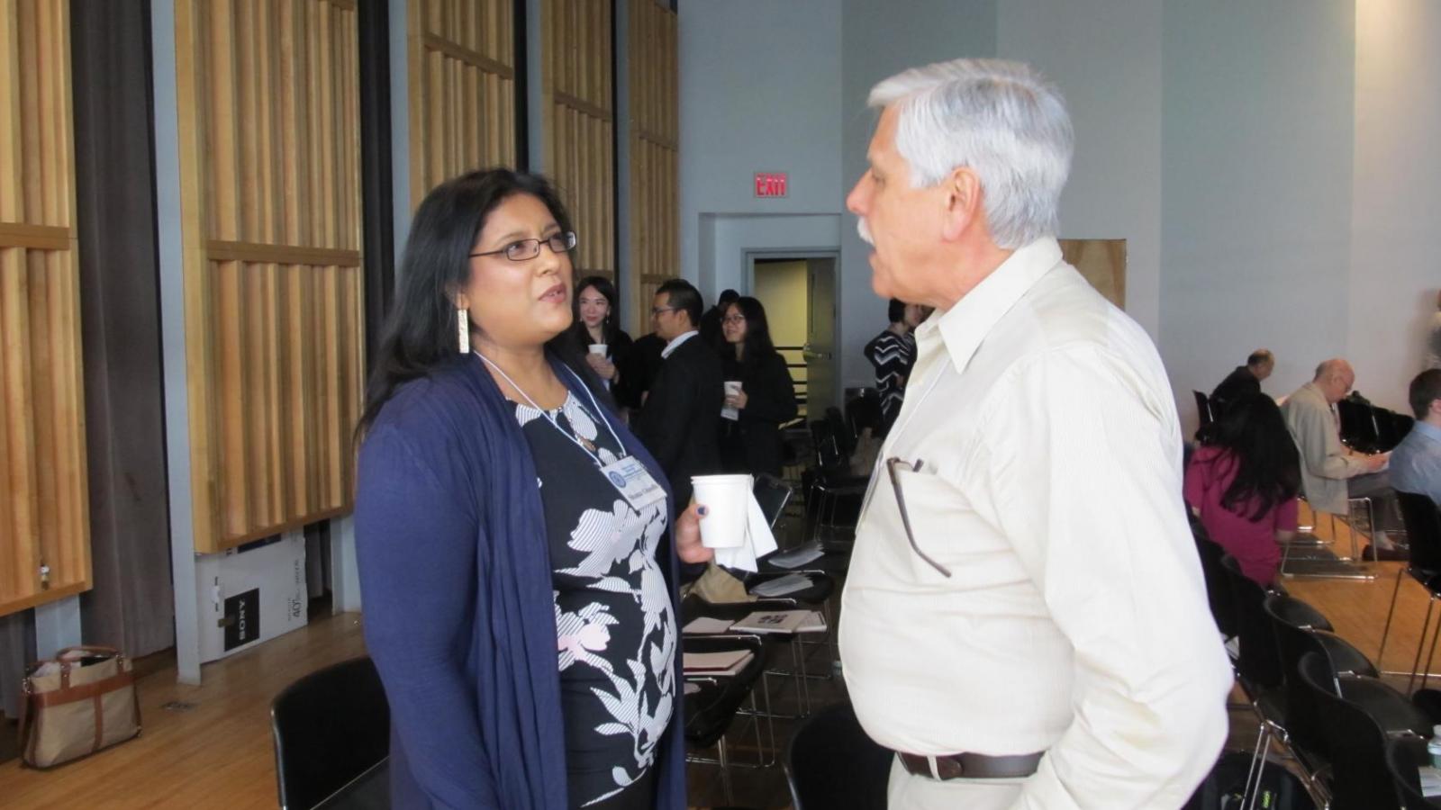 Woman in dark dress clothes and man in light colored dress clothes talking