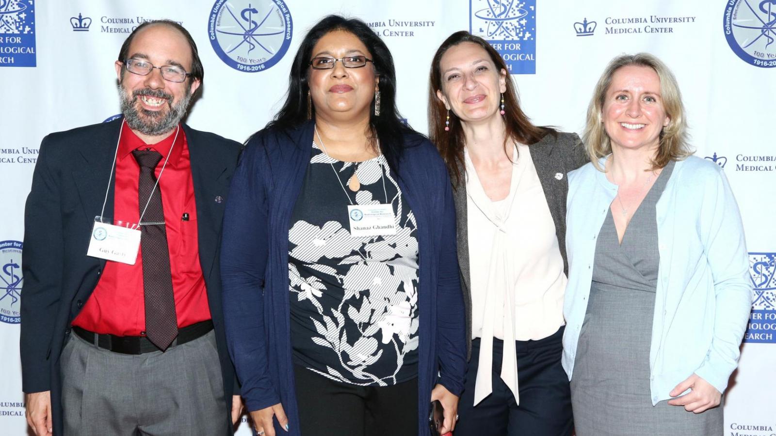 Four people posing for picture in front of back drop with logos