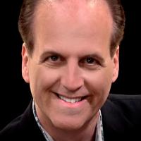 Balding man with dark jacket on posing for headshot