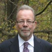 Man in blue suit with glasses and beard posing for head shot