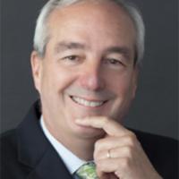 man with gray hair, dark suit jacket, white dress shirt, and green tie posing for headshot with hand up to chin.