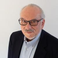 Man in dark suit and light dress shirt with bold dark framed glasses and white hair posing for headshot