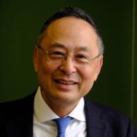 Man with dark hair and glasses wearing blue suit jacket, white dress shirt, and tie posing for headshot