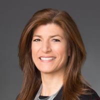 Woman with light brown hair and highlights wearing black dress jacket and shirt with silver necklace in Headshot