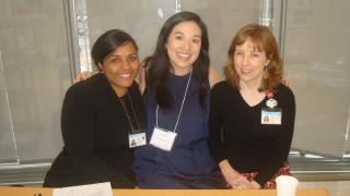 3 female doctors posing for picture seated at wooden table with windows behind them